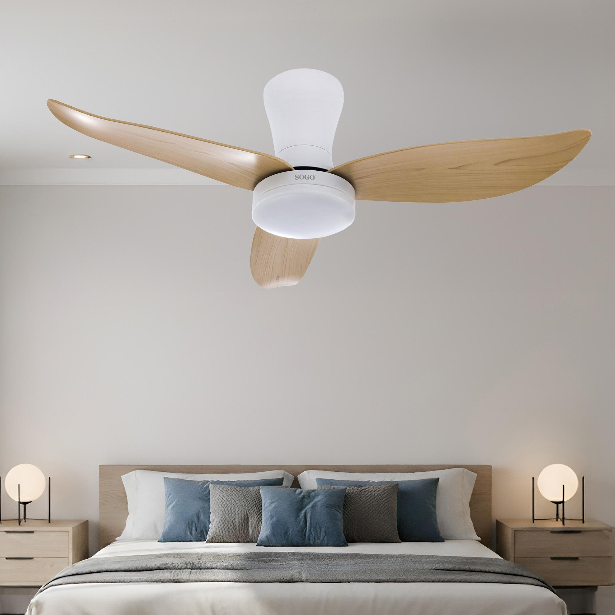 Un ventilatore da soffitto con pale in legno sopra un letto con cuscini blu.