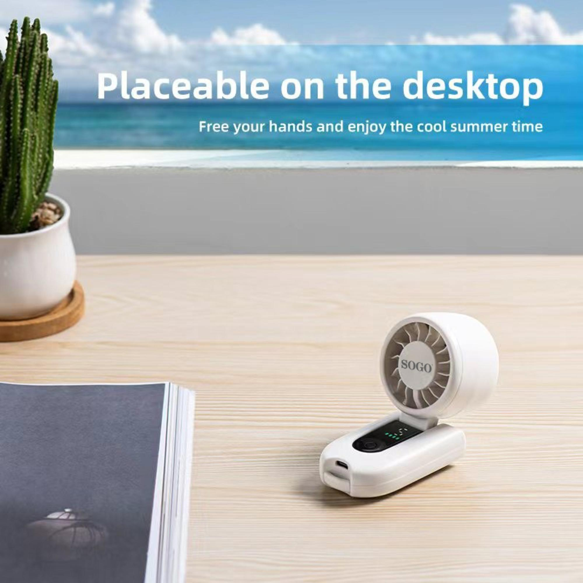 Un ventilador portátil blanco sobre un escritorio de madera junto a un libro y una planta.