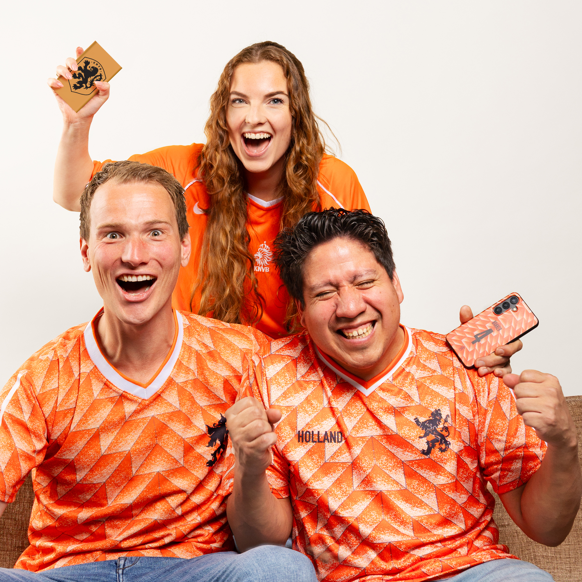Drie fans in oranje shirts juichen voor een witte achtergrond.