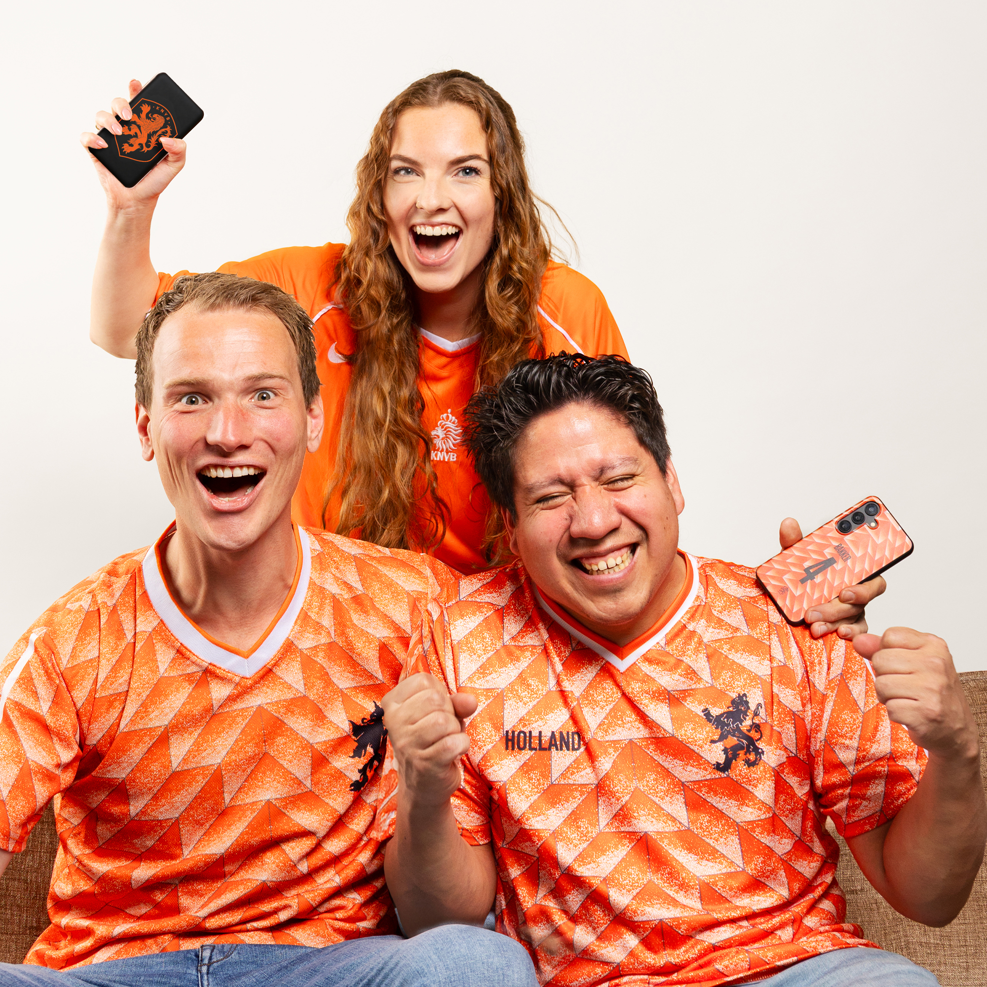 Drie fans in oranje shirts juichen met telefoons in de hand.
