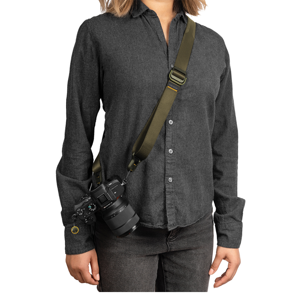 Een persoon in een donkere blouse draagt een camera met groene riem.