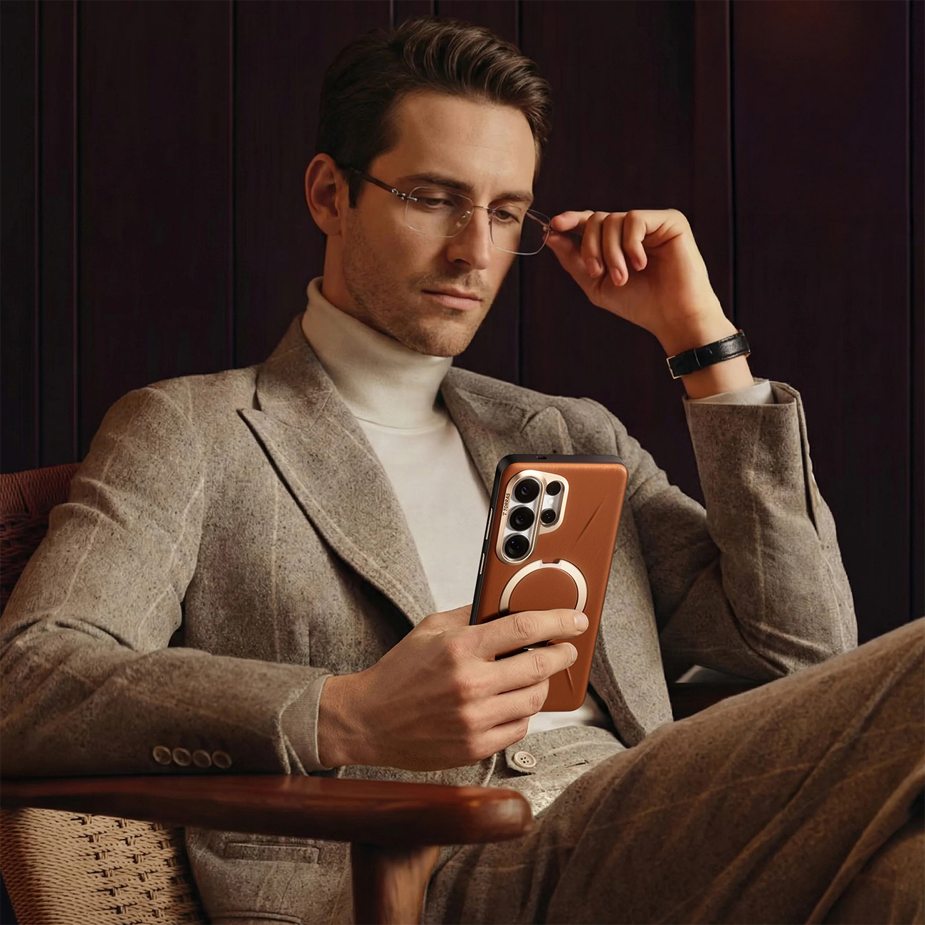 Un hombre con traje se sienta sosteniendo un teléfono con funda de cuero marrón y anillo.