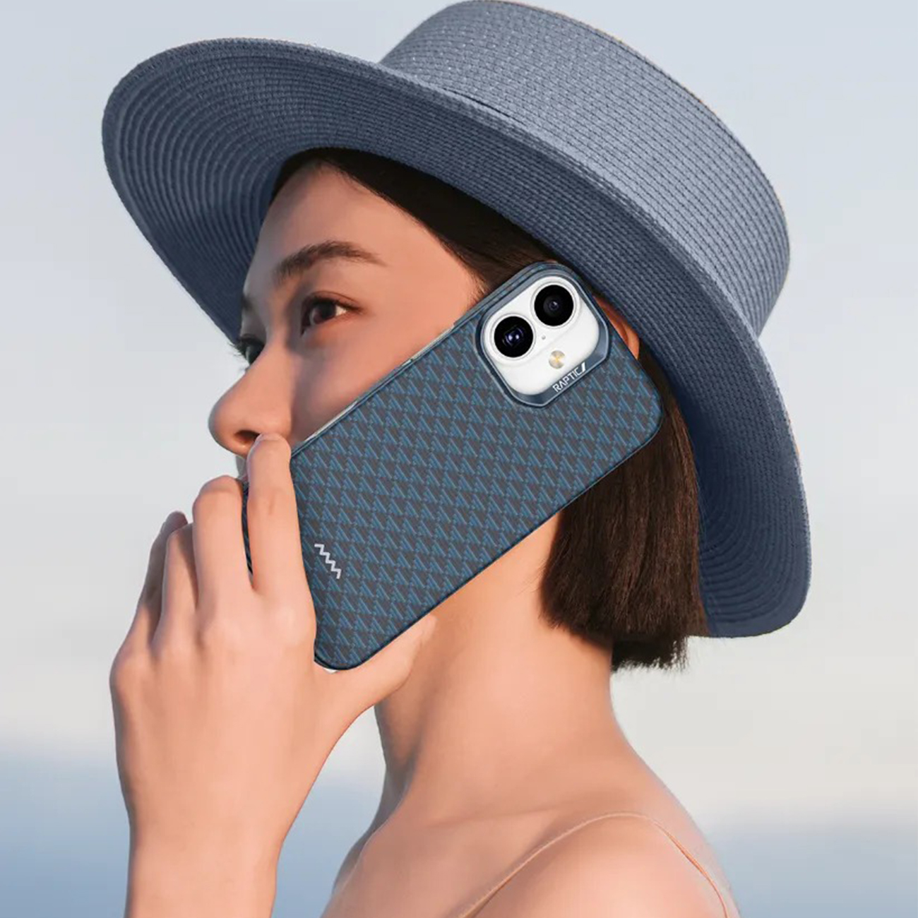 Una mujer con sombrero se lleva un teléfono con estampado a la cara.