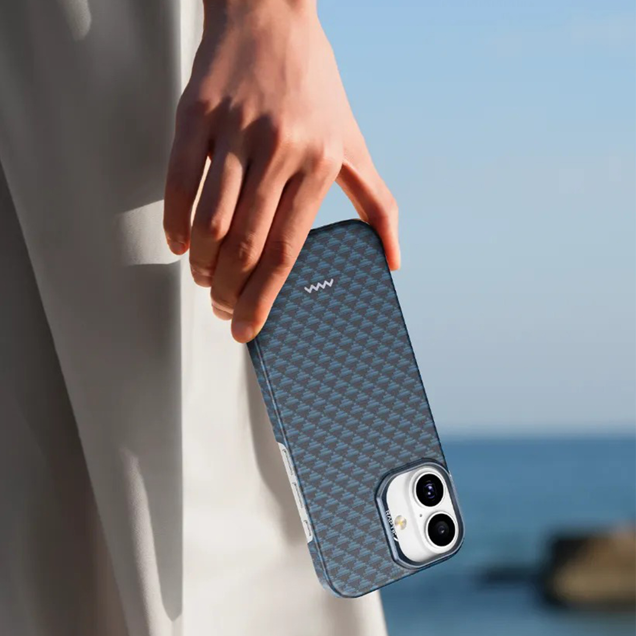 Una mano sostiene un teléfono azul con patrón de cuadros contra un cielo azul.