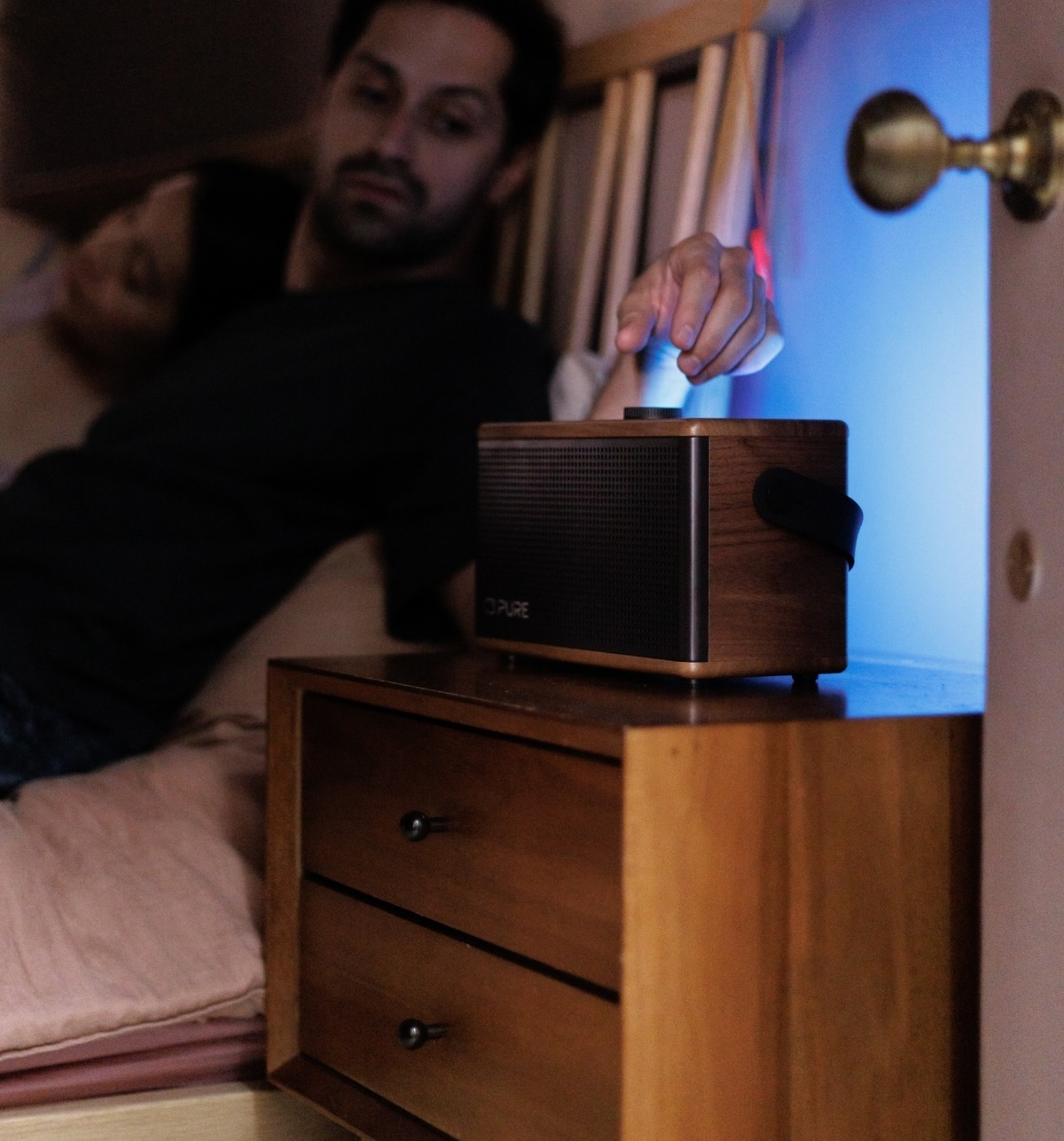 Homme touche radio à côté de couple dormant dans chambre. Lumière bleue.