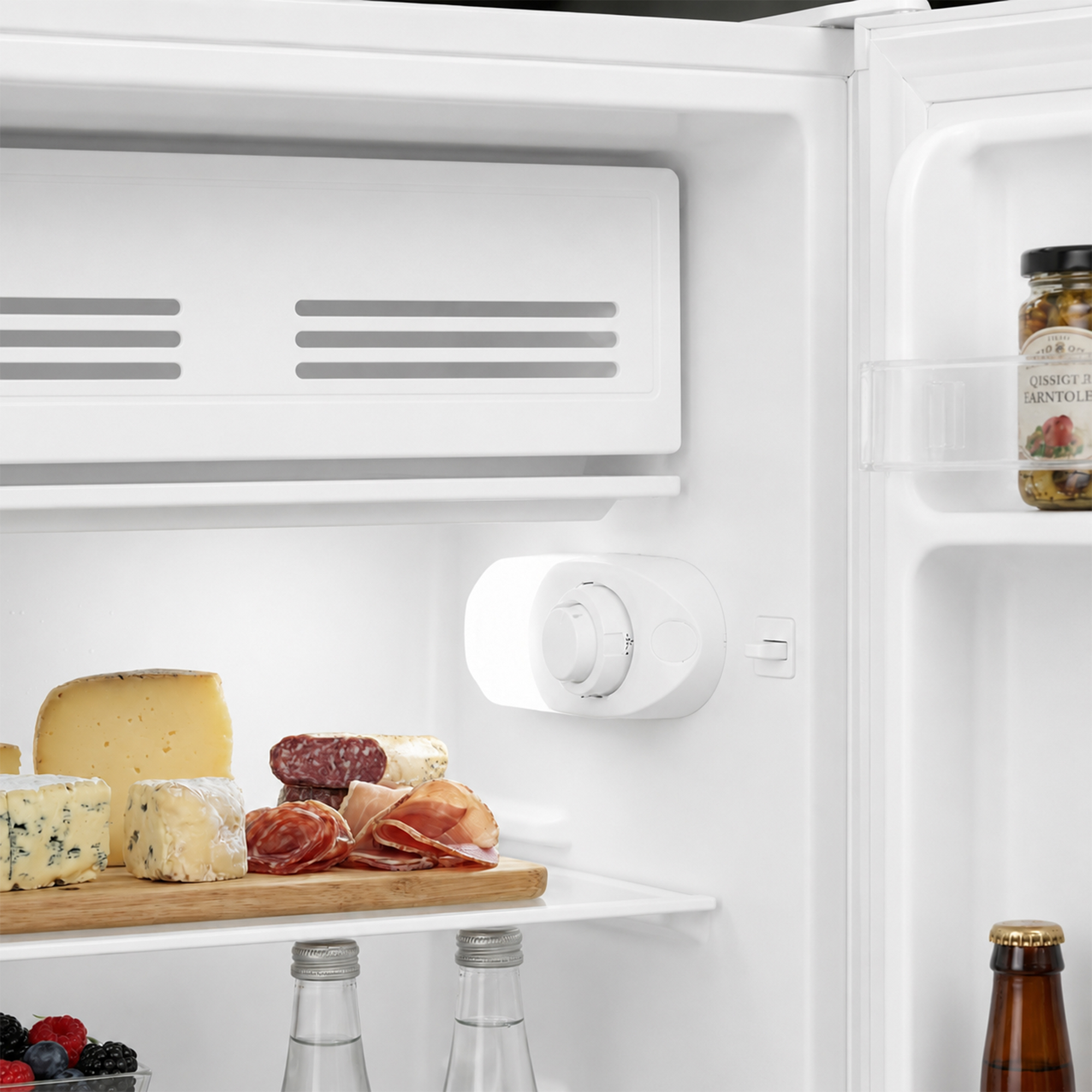 Un réfrigérateur ouvert avec du fromage, de la charcuterie et un bocal de légumes marinés.