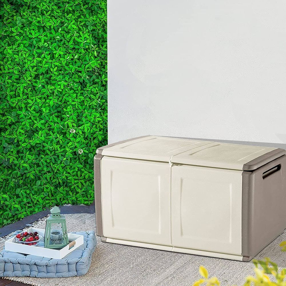 Un baúl de almacenamiento beige con ribete marrón está sobre una alfombra junto a una pared verde y blanca.