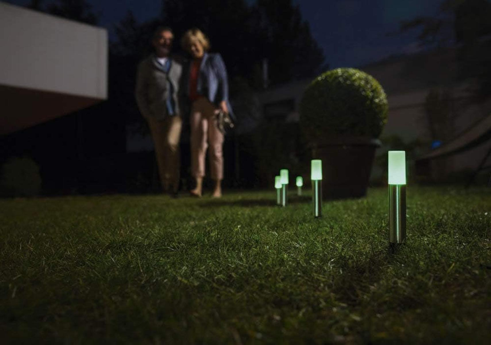 Paar spaziert nachts auf dem Rasen mit leuchtenden Gartenlichtern.