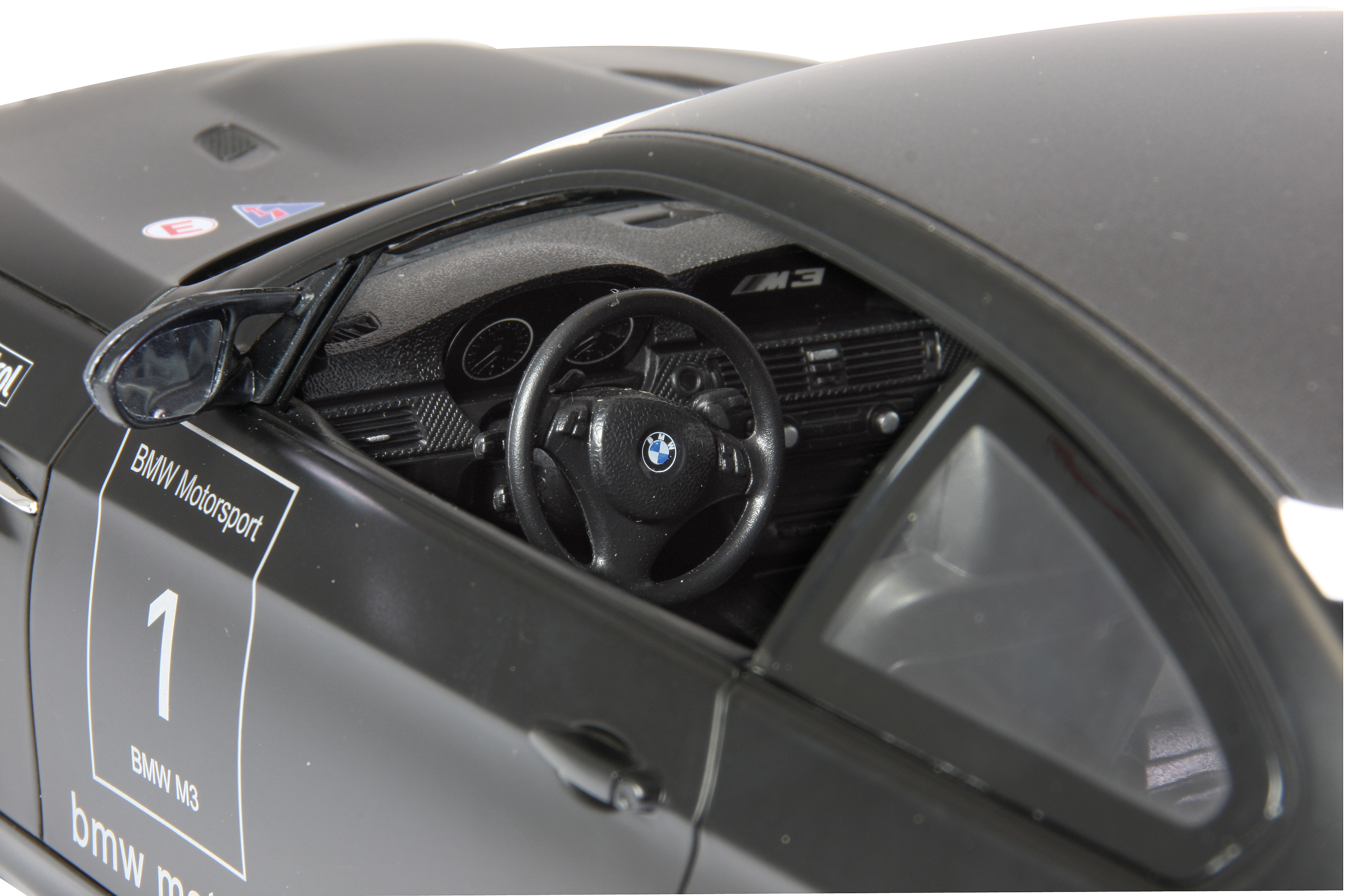 Czarny BMW M3 z numerem 1, wnętrze z kierownicą i deską rozdzielczą.