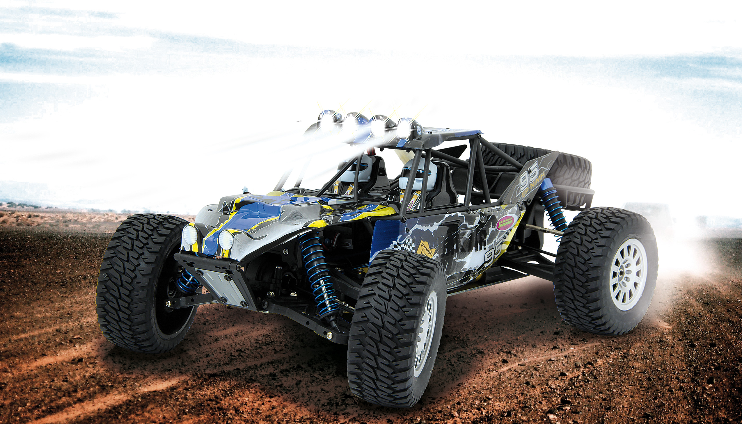 Ein blau-gelber ferngesteuerter Buggy mit hellen Scheinwerfern auf einer Sandpiste.