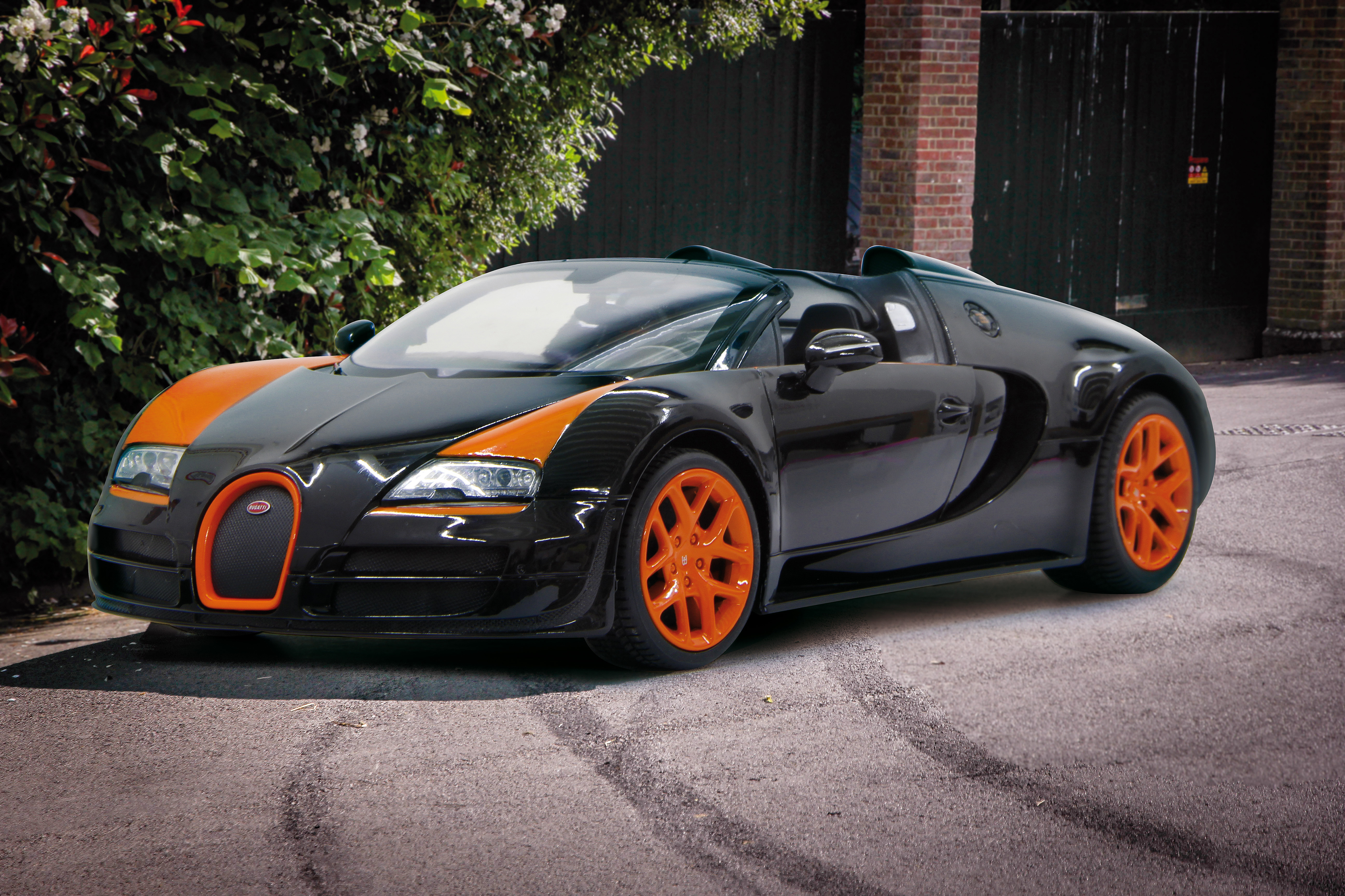 Schwarzer Bugatti mit orangefarbenen Akzenten und Felgen, geparkt auf Asphalt.