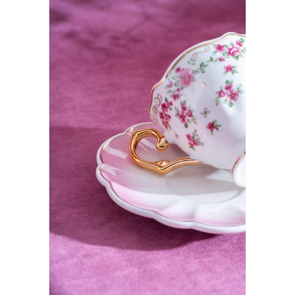 Pembe çiçekli, altın kulplu beyaz çay fincanı pembe bir tabağın üzerinde.