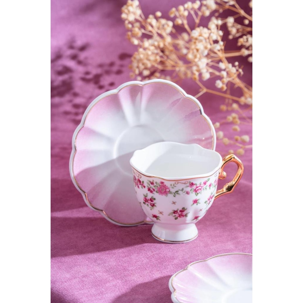 Altın kulplu, pembe çiçekli, narin porselen çay fincanı, pembe fincan tabağında duruyor.