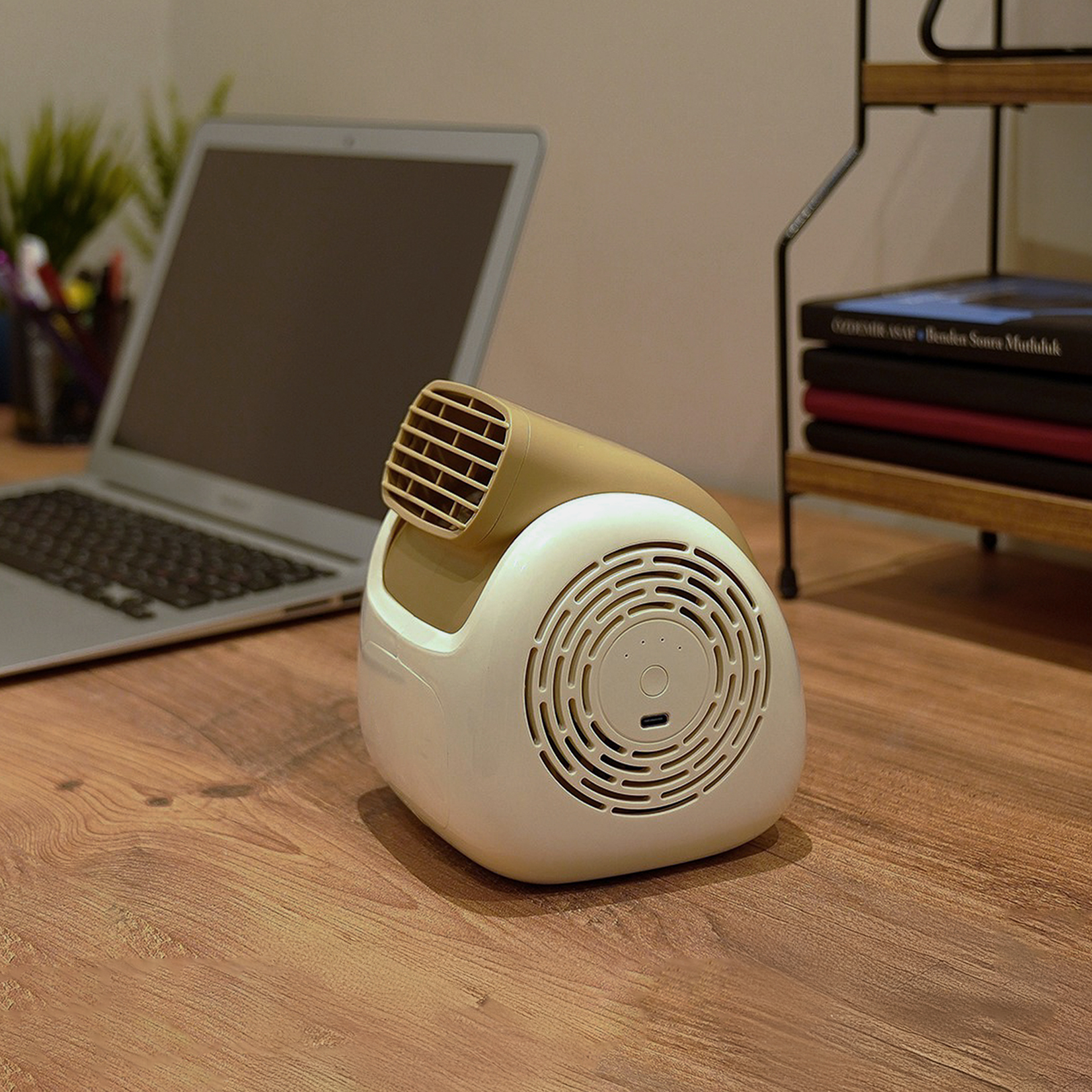 Bej ve beyaz mini fan, dizüstü bilgisayarın yanında ahşap bir masada duruyor.