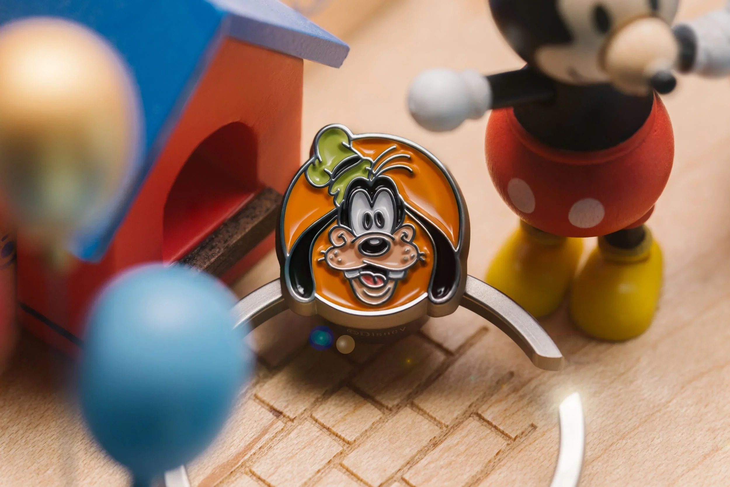 Una spilla di Pluto è al centro, con Topolino e una casa giocattolo dietro.