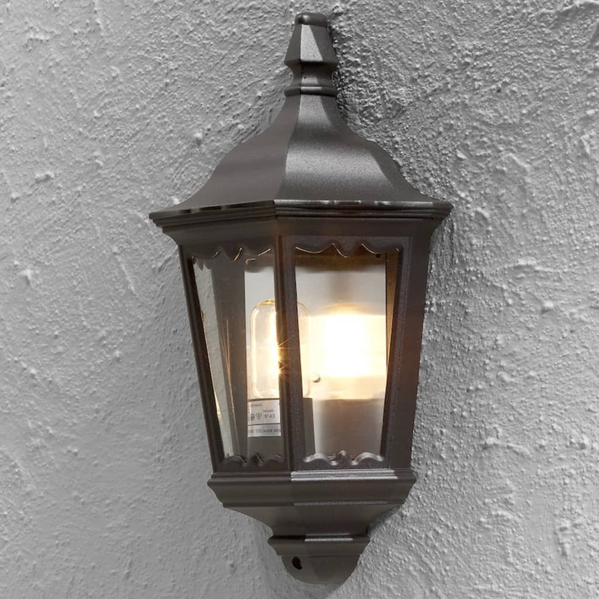 Dunkelgraue Wandlaterne mit Glas und Glühbirne an einer strukturierten weißen Wand.