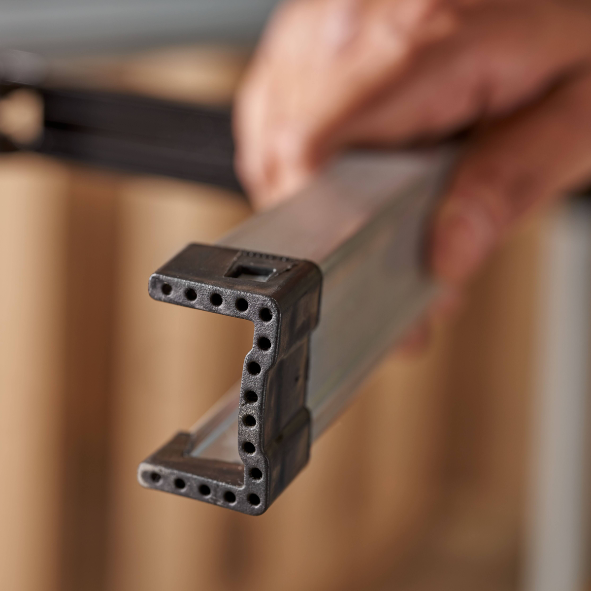 Eine Hand hält ein Metallprofil mit schwarzen Endkappen, die viele kleine Löcher aufweisen.