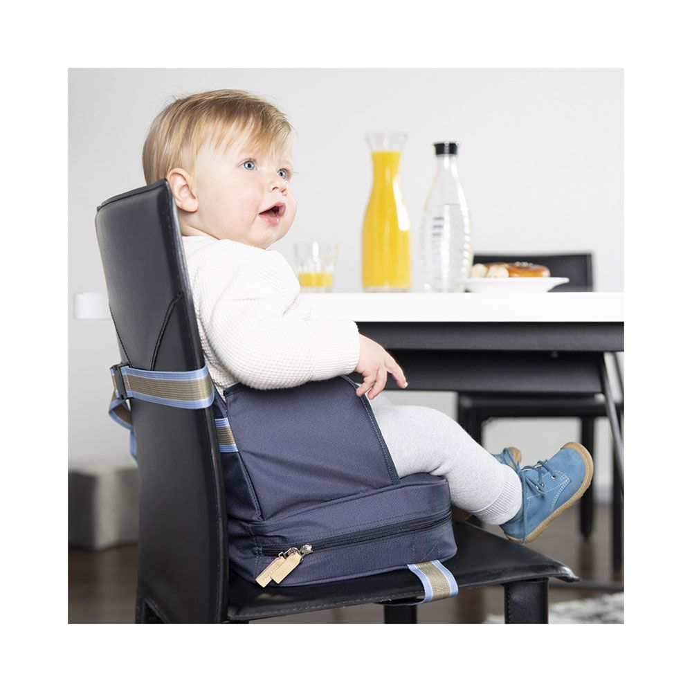 Ein Baby sitzt in einem Hochstuhl auf einem Stuhl am Tisch. Orangensaft und Wasser.