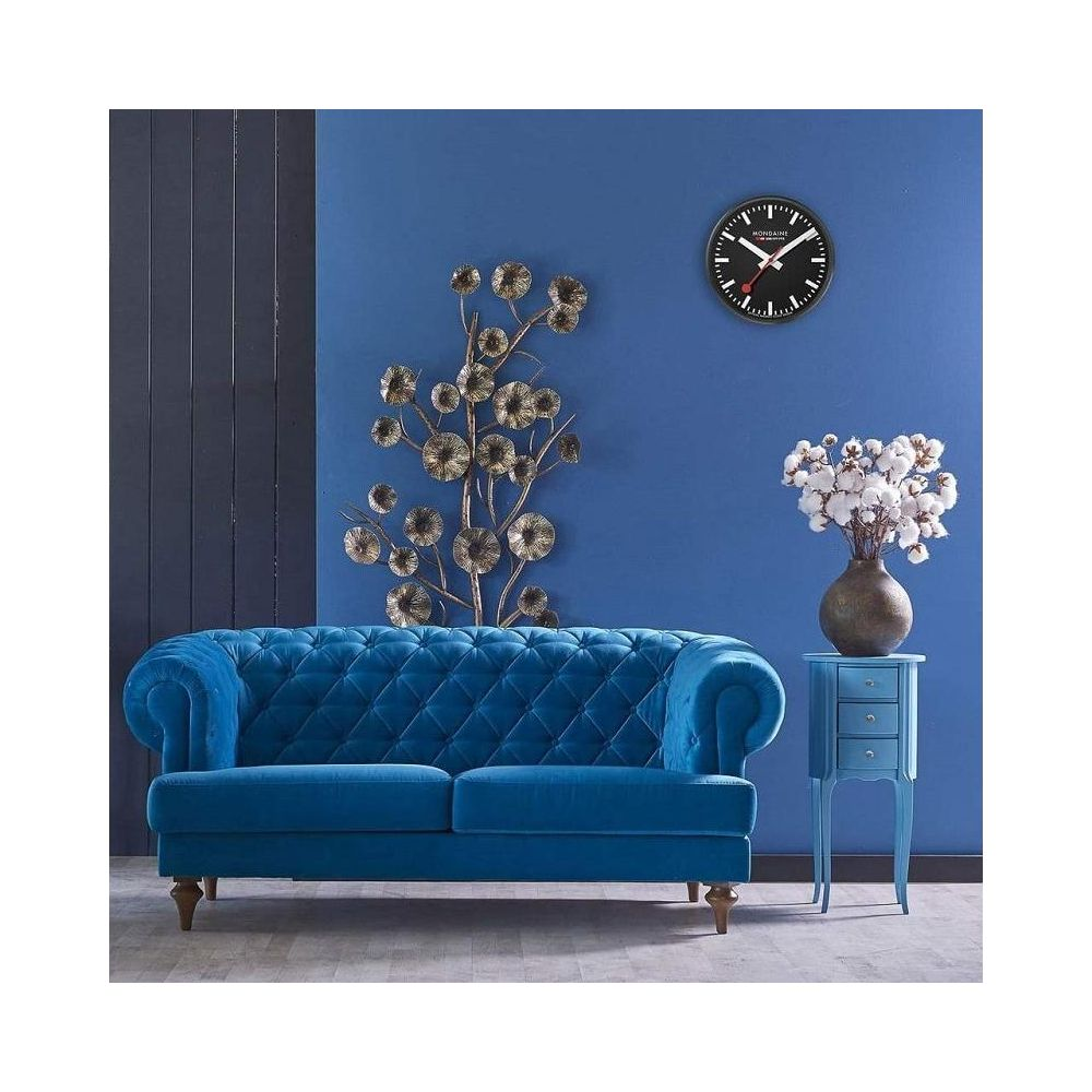 Ein königsblauer Chesterfield-Sofa steht vor einer blauen Wand mit Wanddeko und einer Vase mit Baumwollblüten.