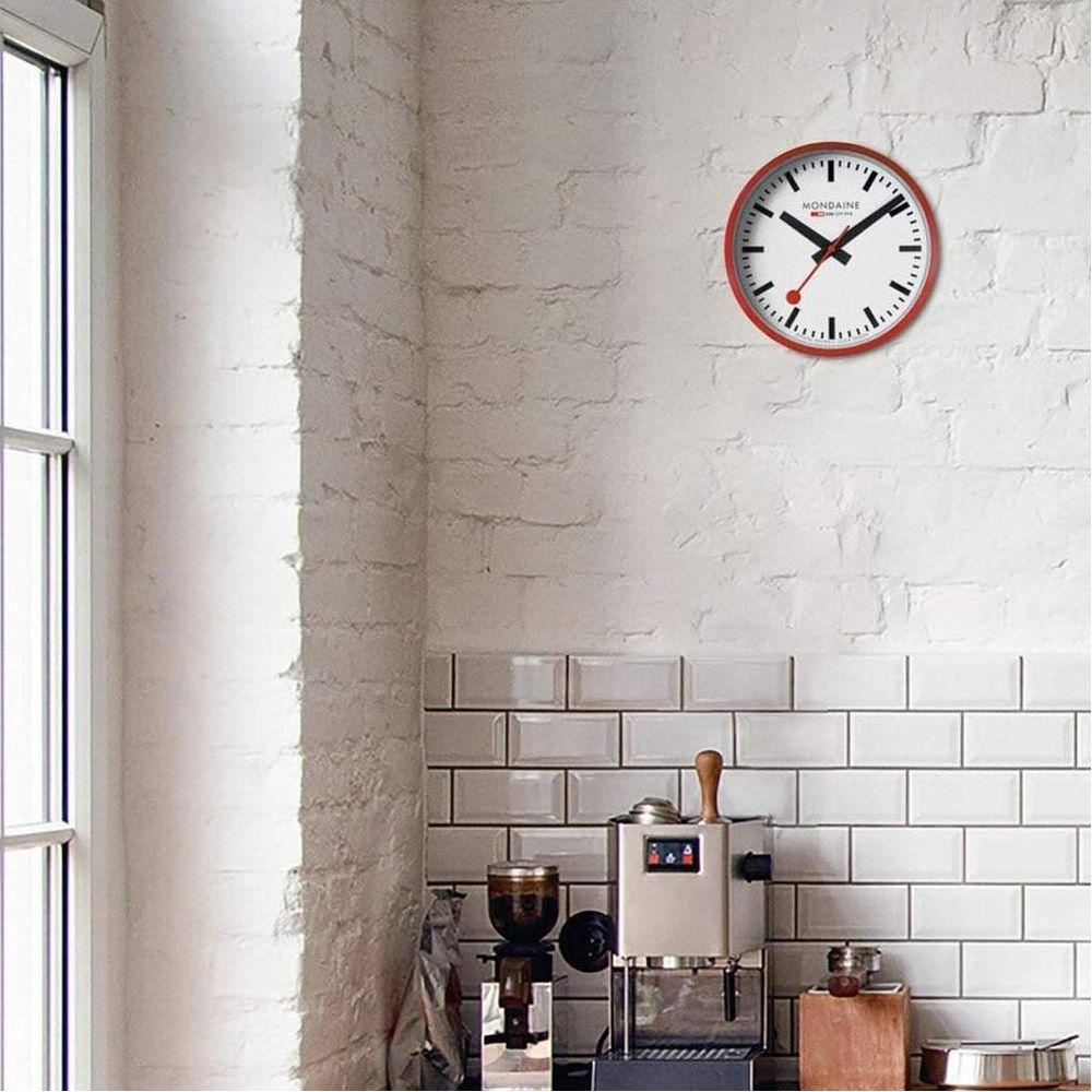 Un orologio con cornice rossa è appeso a un muro di mattoni bianchi sopra una macchina da caffè.