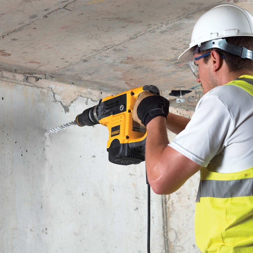 Ein Mann mit Helm bohrt mit einem gelben Bohrer in eine Betonwand.
