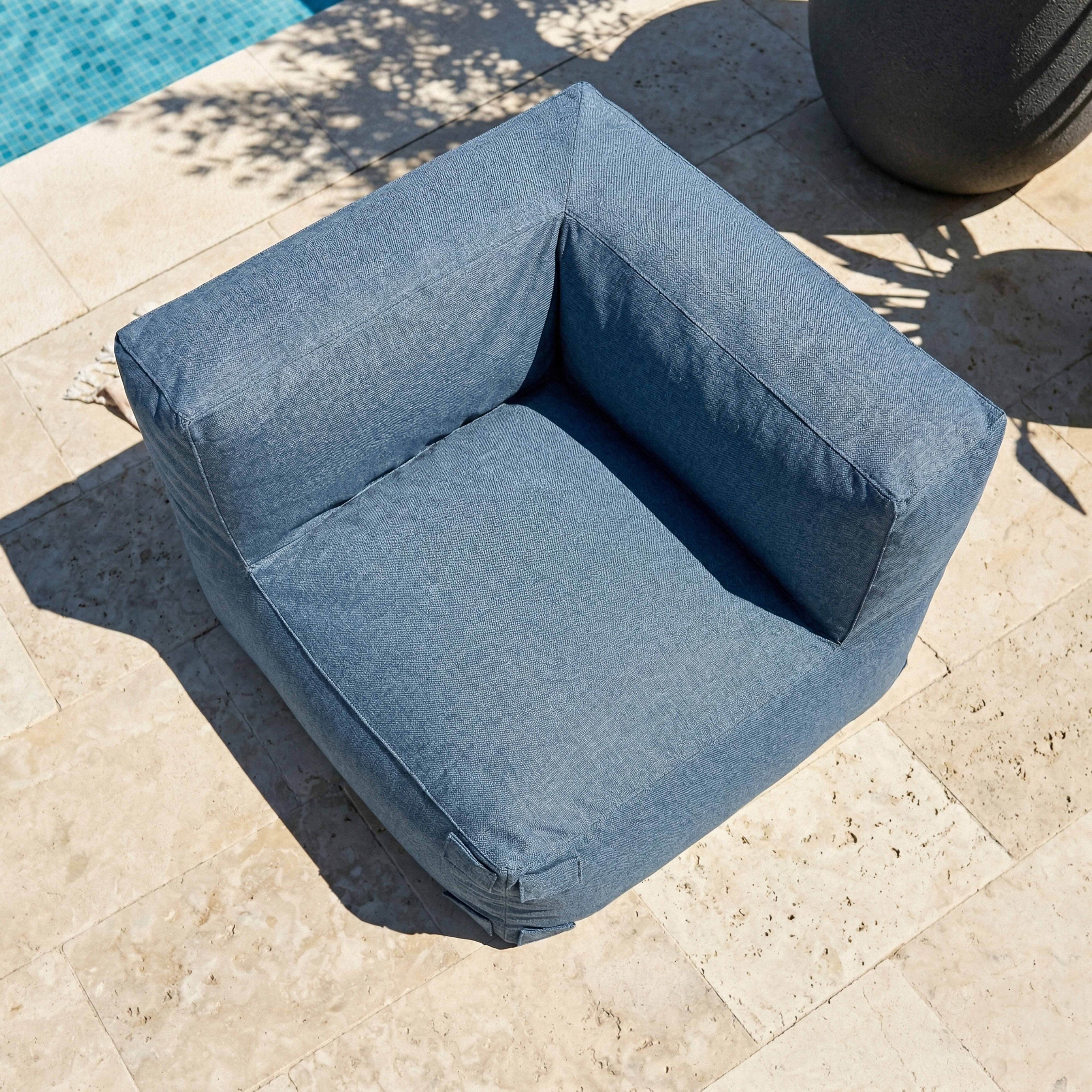 Ein blauer Sessel steht auf einer beigen Steinterrasse neben einem Pool.