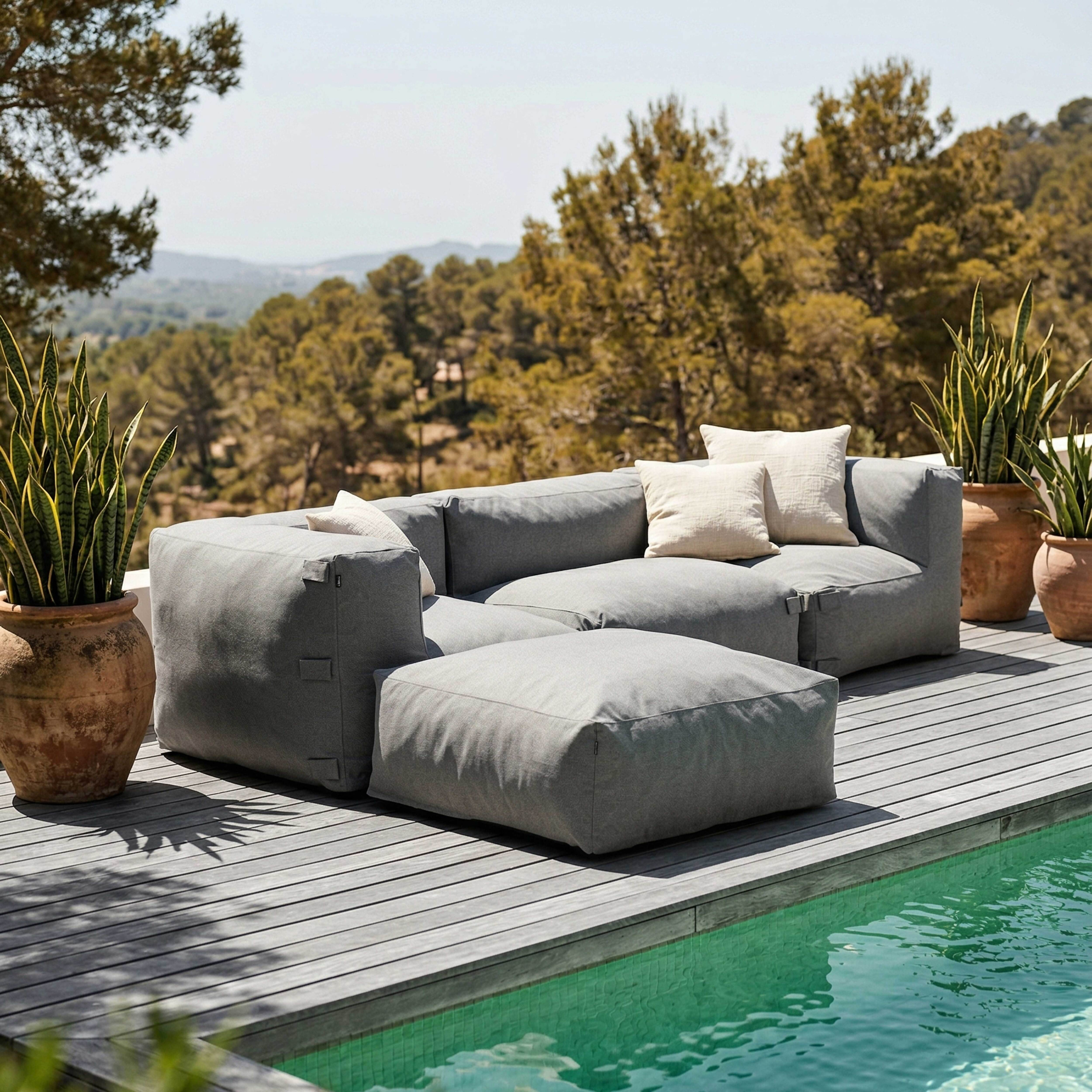 Graue Outdoor-Möbel am Pool mit Pflanzen und Hügeln im Hintergrund.