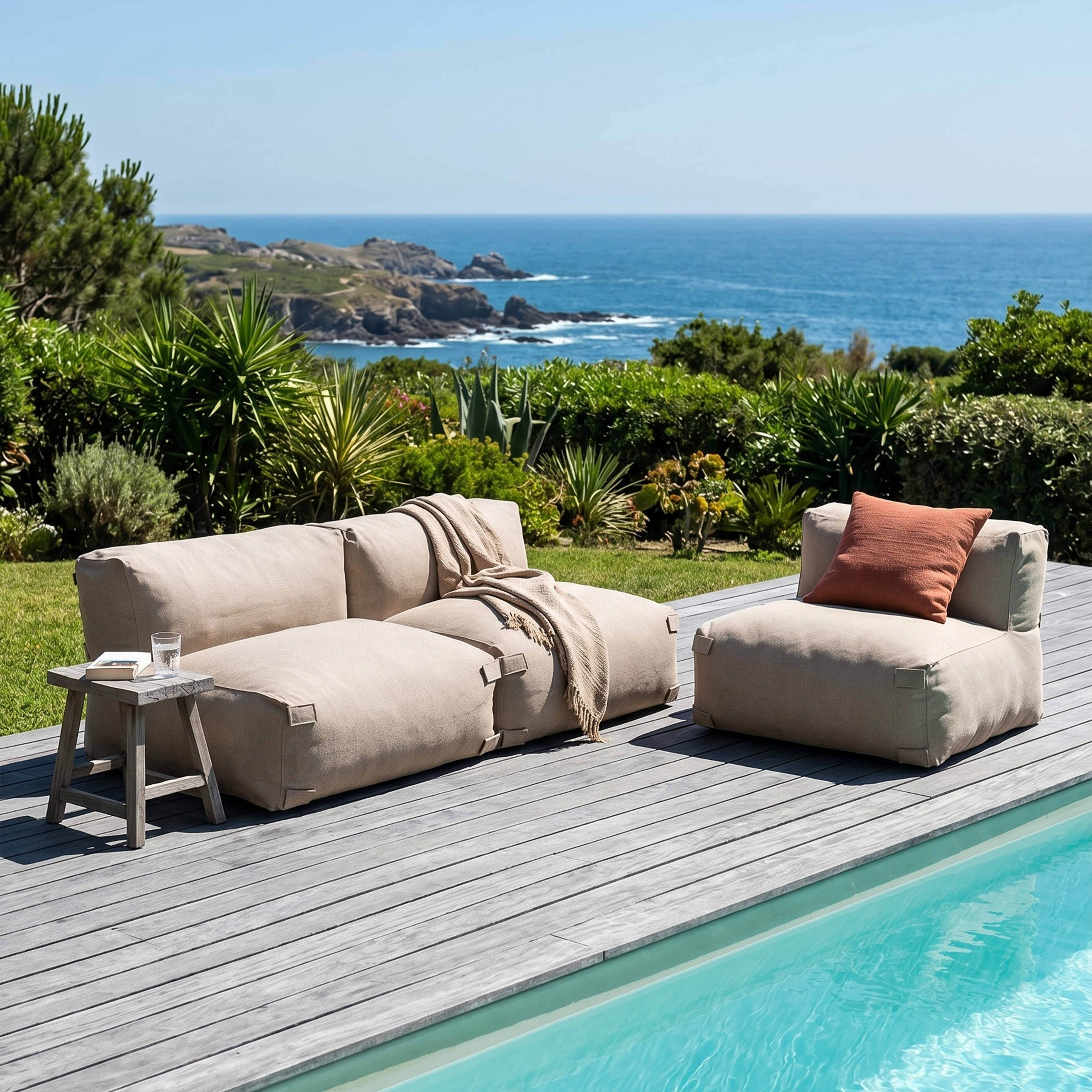Beige Loungemöbel am Pool mit Blick auf das Meer und Felsen.
