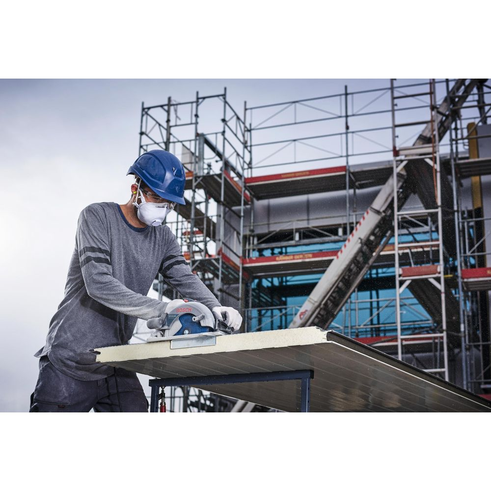 Mann mit Helm und Maske schneidet mit Kreissäge Metallplatte auf Baustelle.