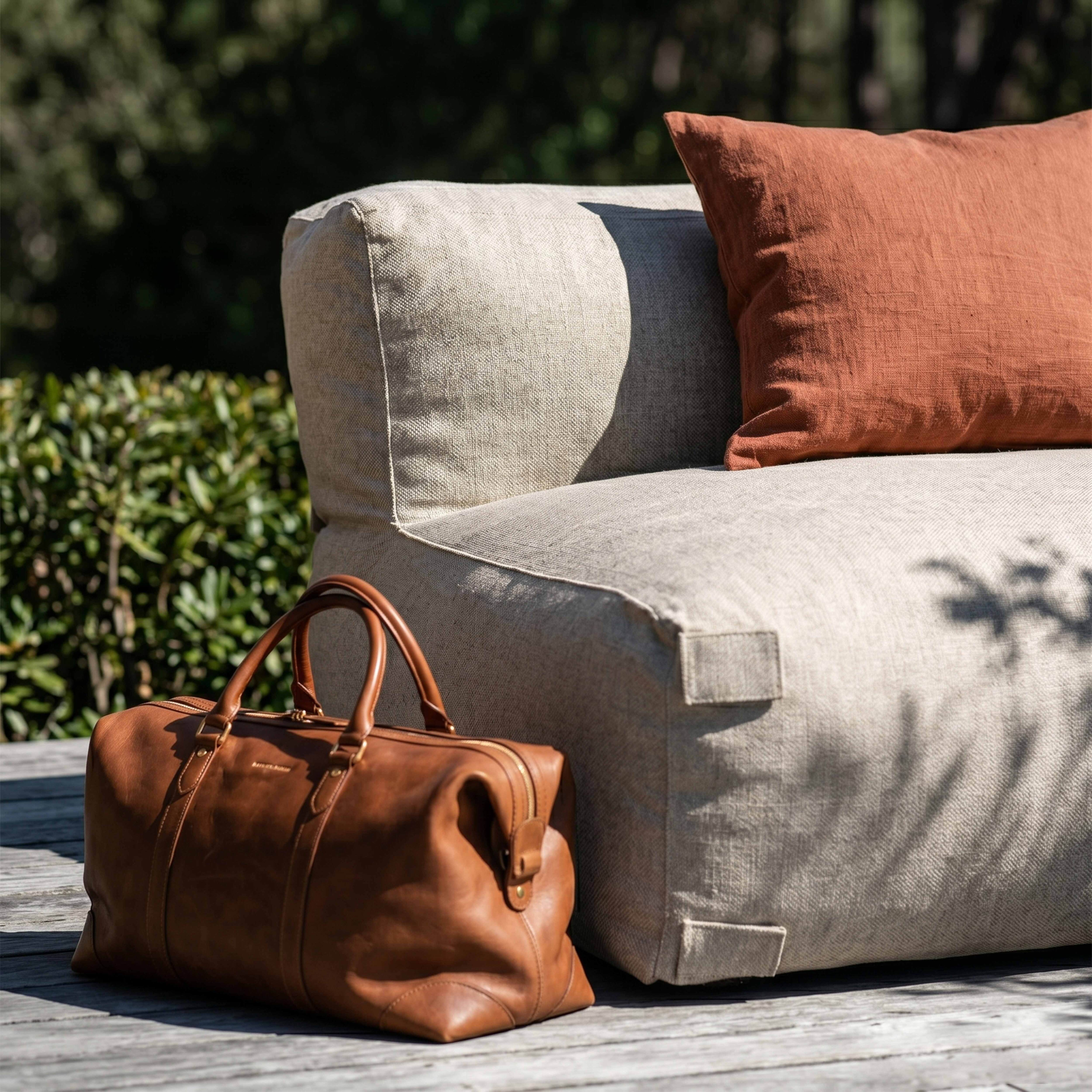 Eine braune Ledertasche steht neben einem beigefarbenen Sitzsack mit einem orangefarbenen Kissen.