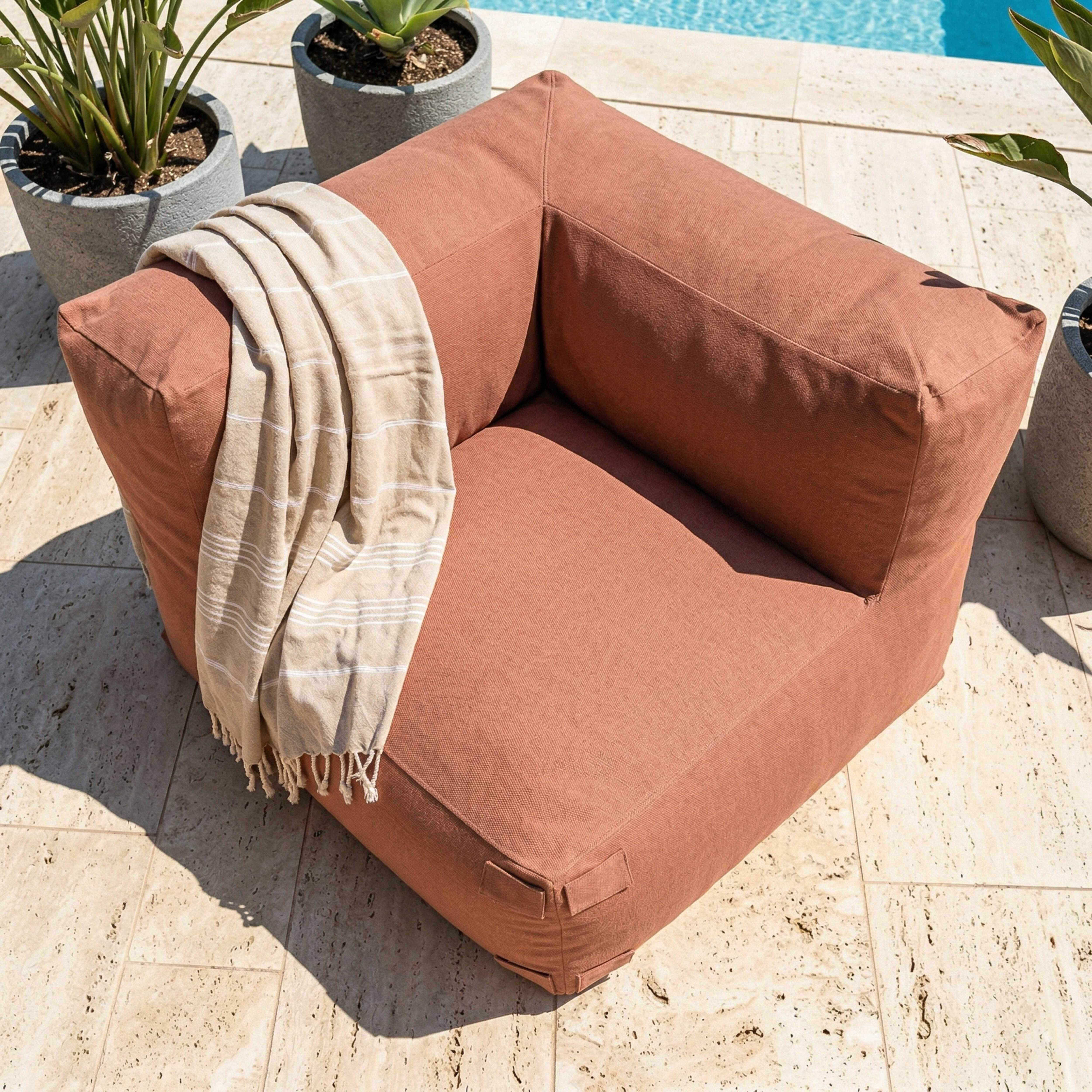 Ein korallenfarbener Sitzsack mit einer Decke daneben, am Pool.