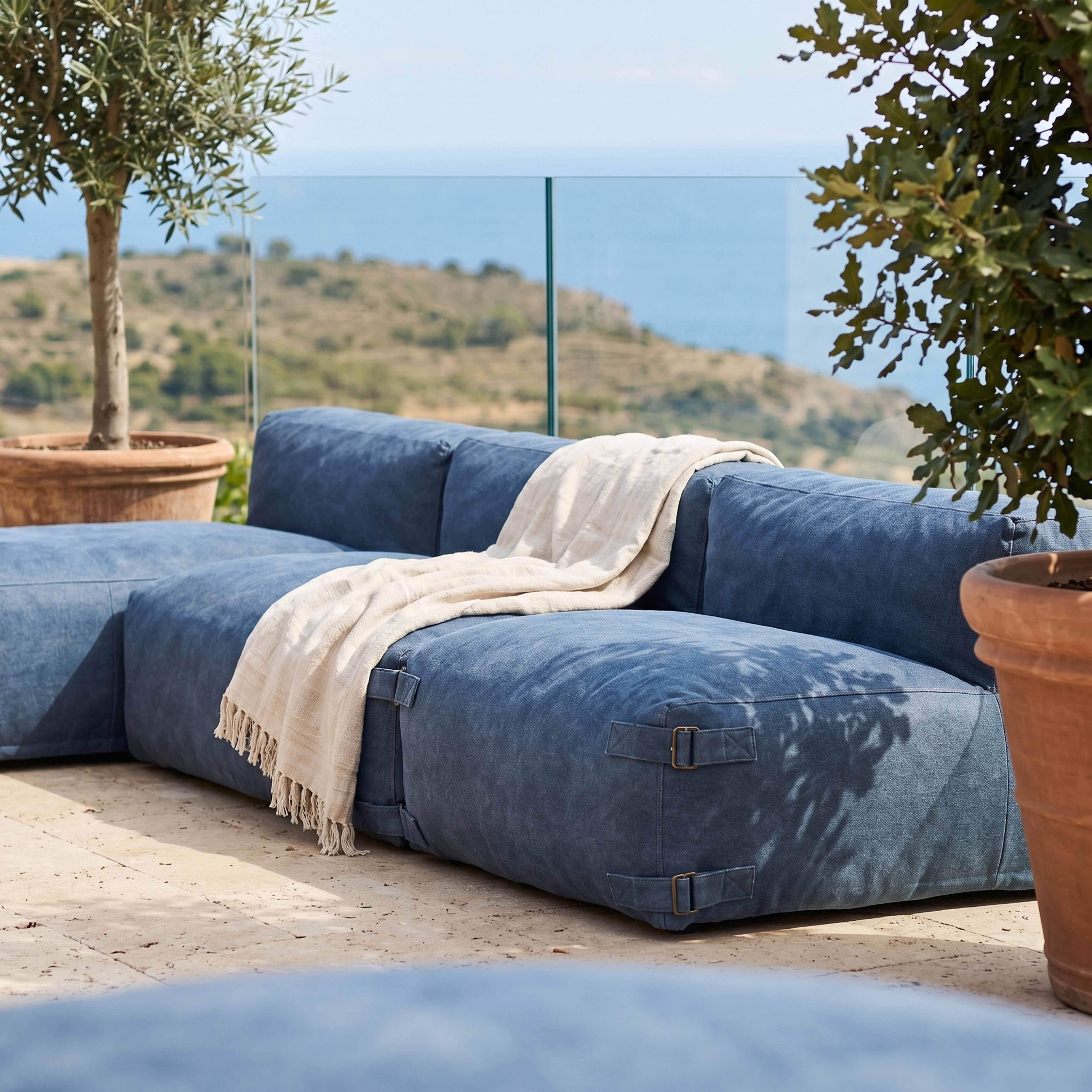 Ein blaues Sofa mit einer Decke im Freien, mit Bäumen und Meer im Hintergrund.