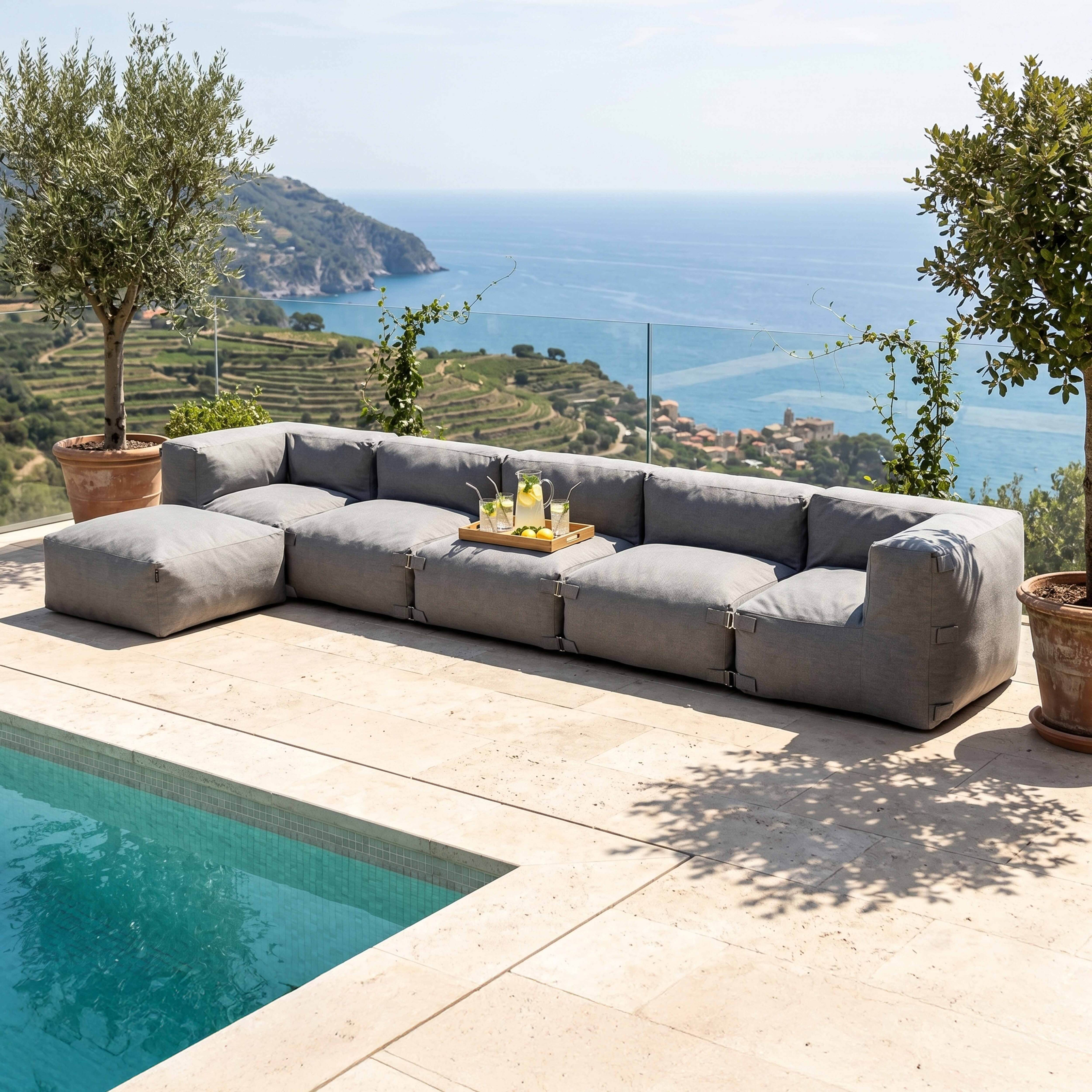 Graues Outdoor-Sofa am Pool mit Blick auf das Meer und terrassierte Hänge.