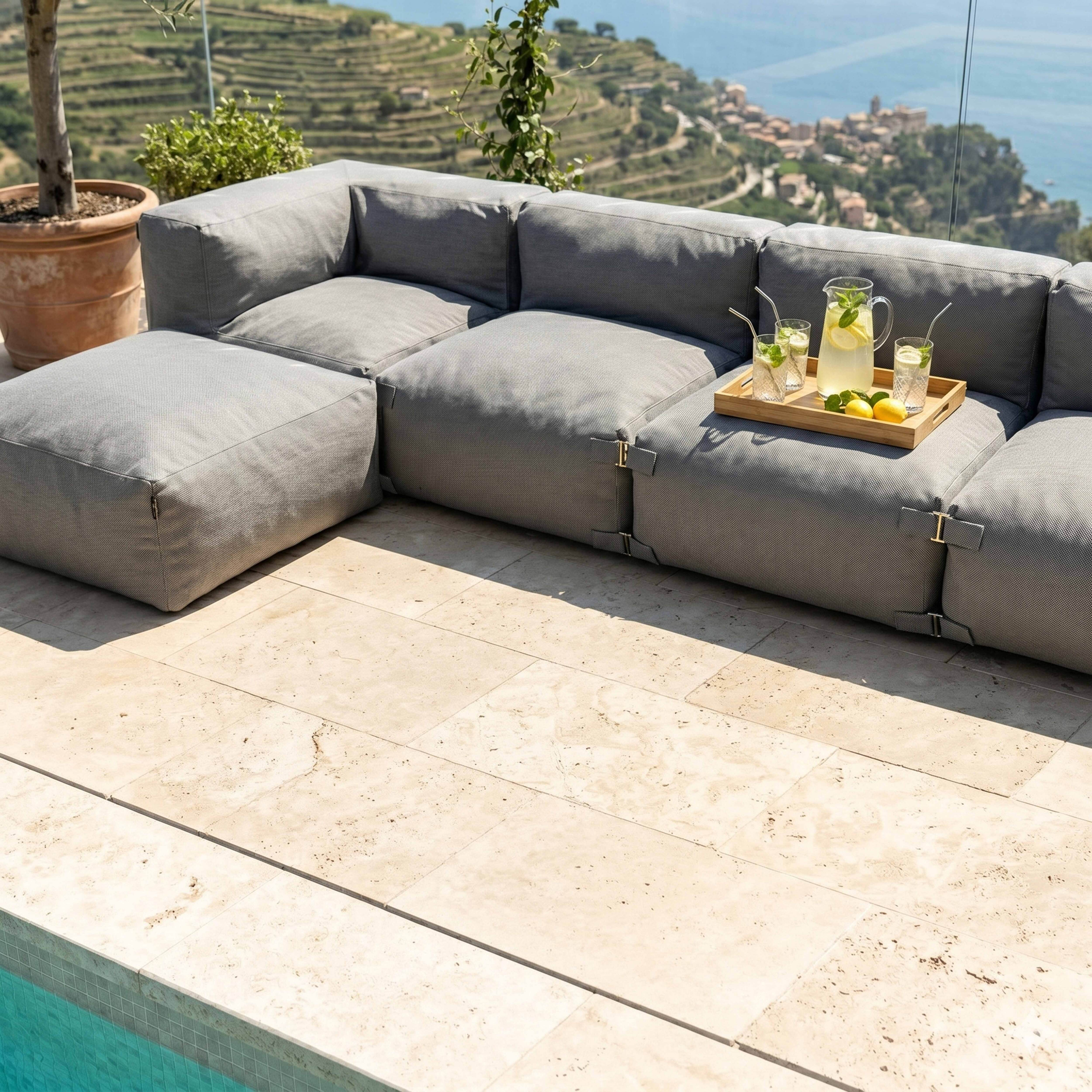 Graues Outdoor-Sofa mit Getränken am Pool, Blick auf eine Küstenstadt.