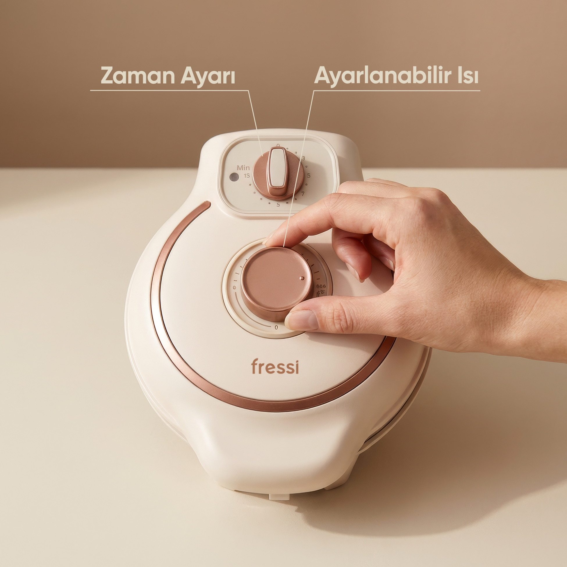 Bir el, rose gold detaylı krem rengi bir cihazın düğmesini çeviriyor.