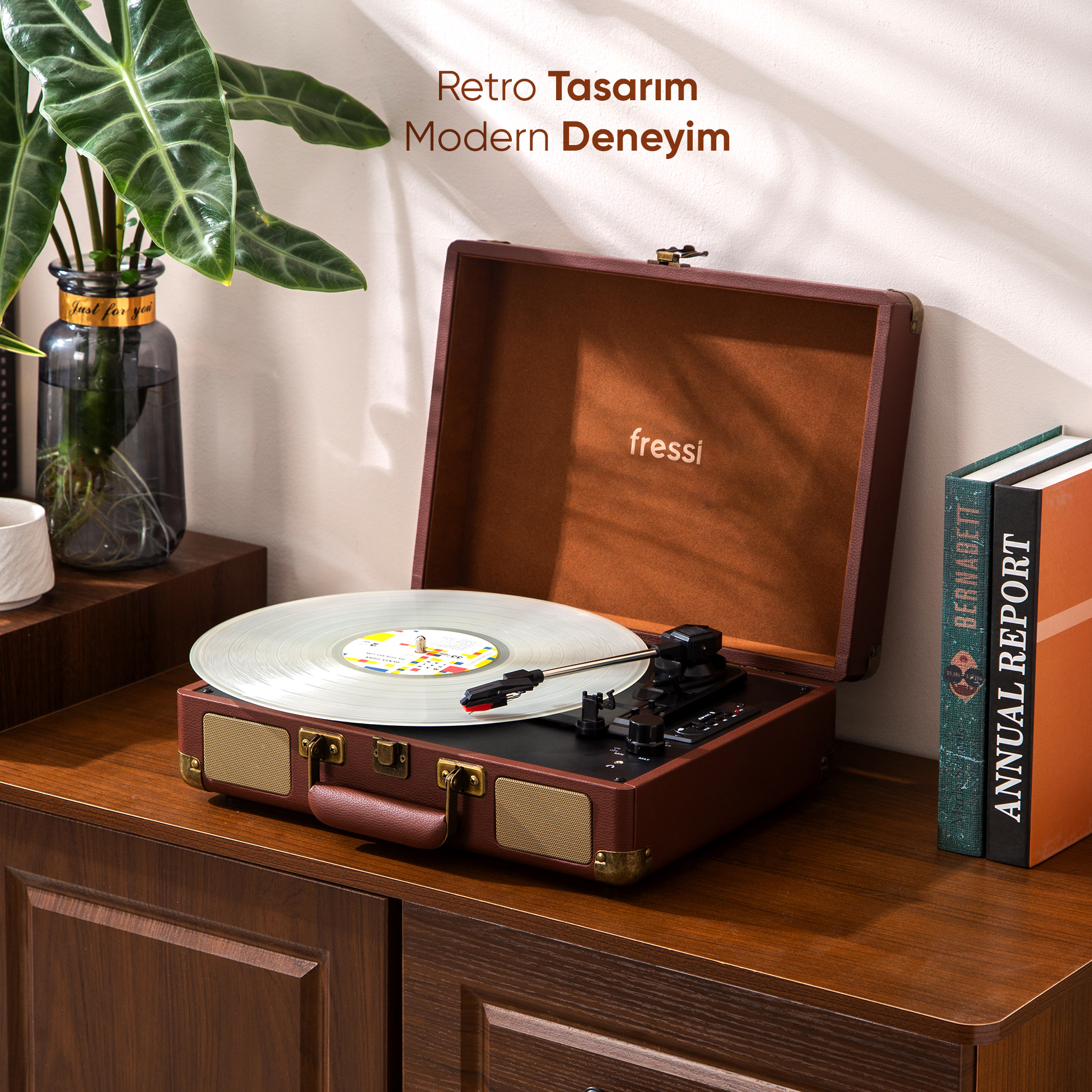 Vinil plaklı kahverengi pikap, kitaplar ve bitkinin yanında ahşap bir dolap üzerinde duruyor.