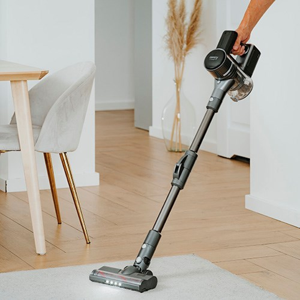 Ręka trzyma odkurzacz bezprzewodowy, odkurzając dywan w pokoju.
