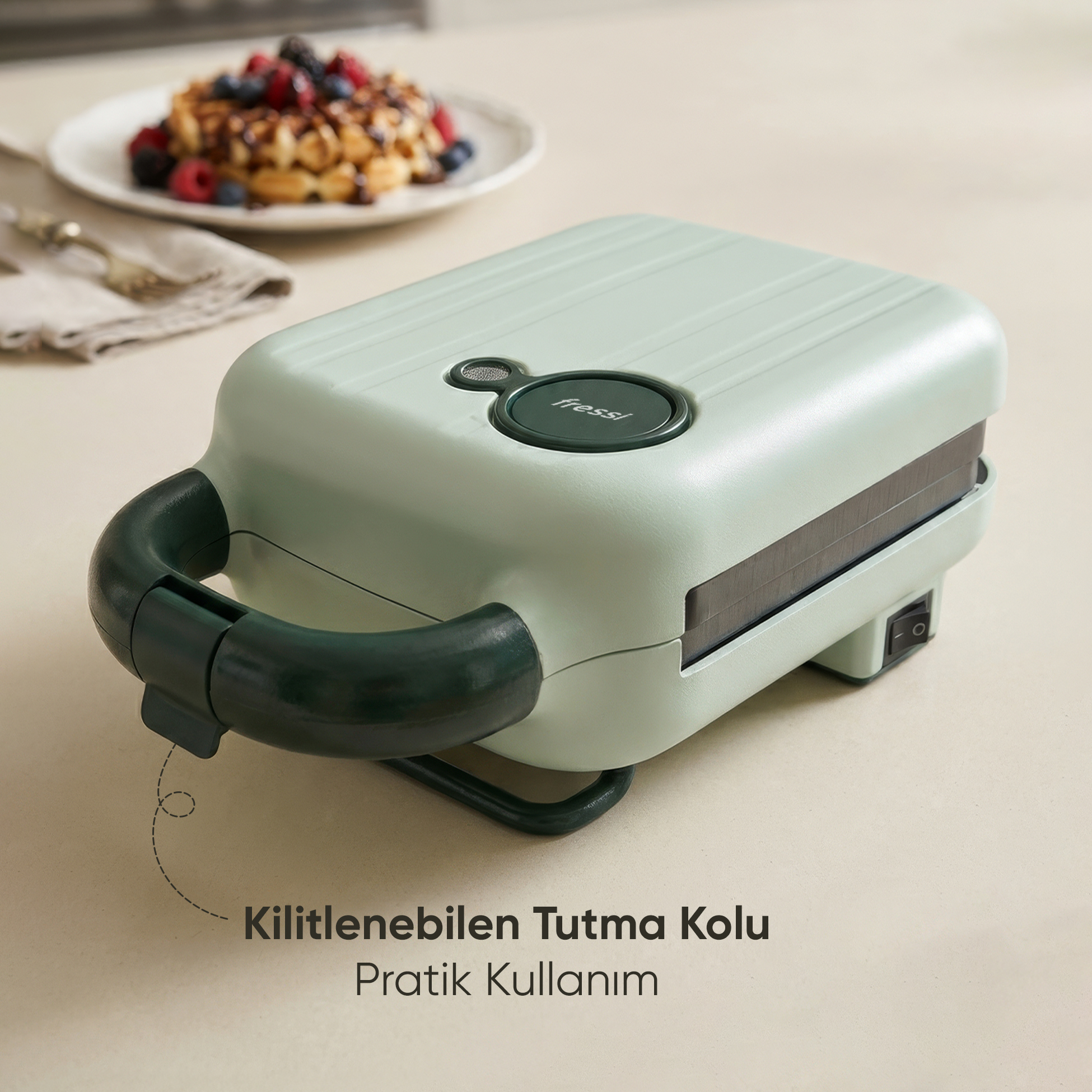 Koyu kulplu, açık yeşil waffle makinesi. Arkada waffle yemeği.
