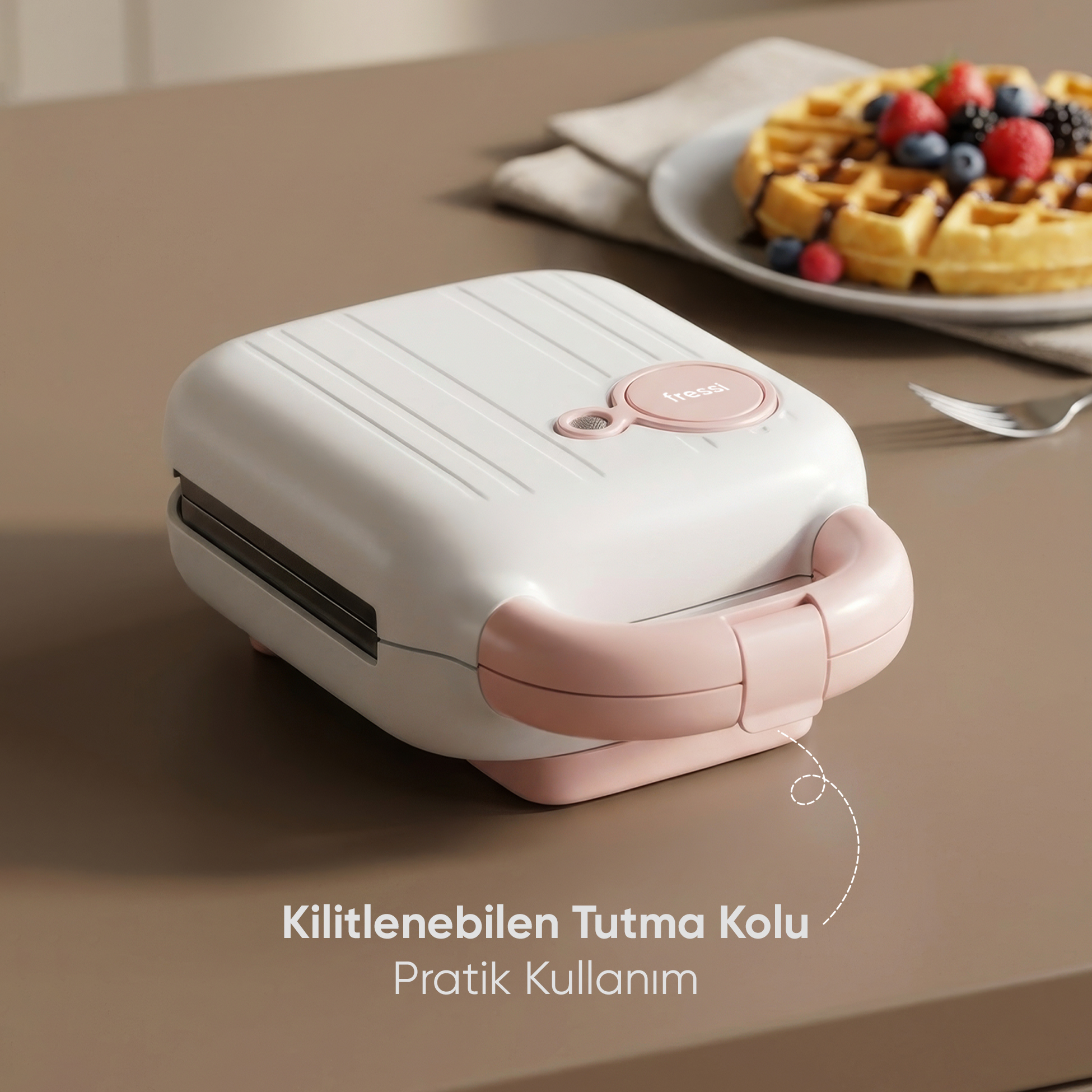 Beyaz ve pembe waffle makinesi masada duruyor, yanında waffle tabağı var.