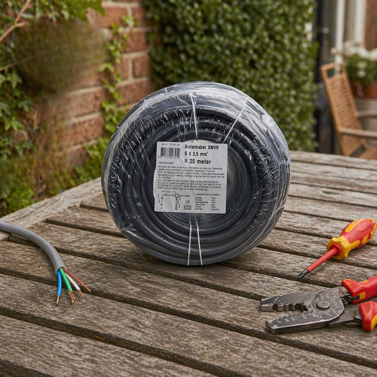 Un rouleau de câble noir sur une table en bois avec des outils et un fil dénudé.