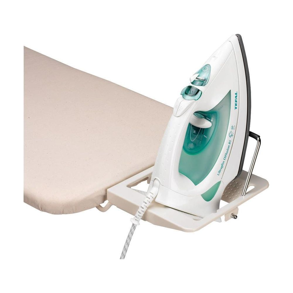 Un fer à repasser Tefal blanc et turquoise repose sur un support en plastique à côté d'une planche à repasser.