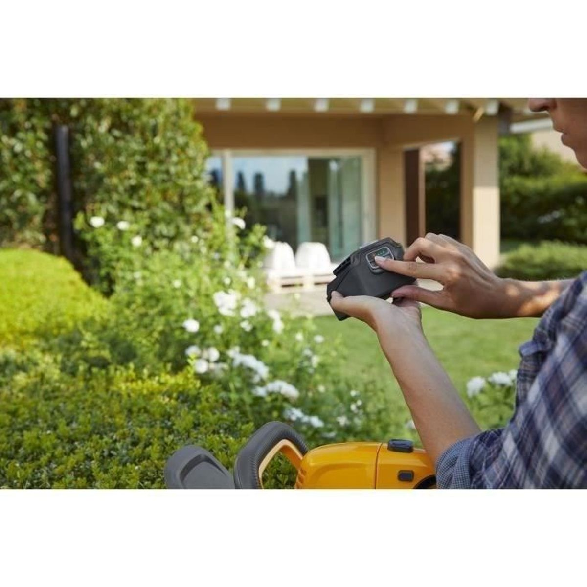 Person setzt Akku in gelben Rasenmäher im Garten ein.