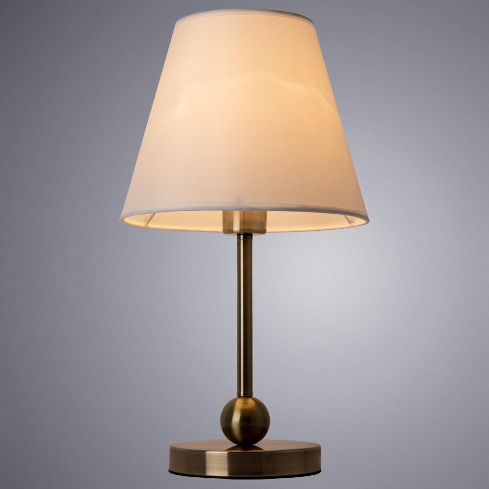 Eine Tischlampe mit einem cremefarbenen Lampenschirm und einem messingfarbenen Sockel.