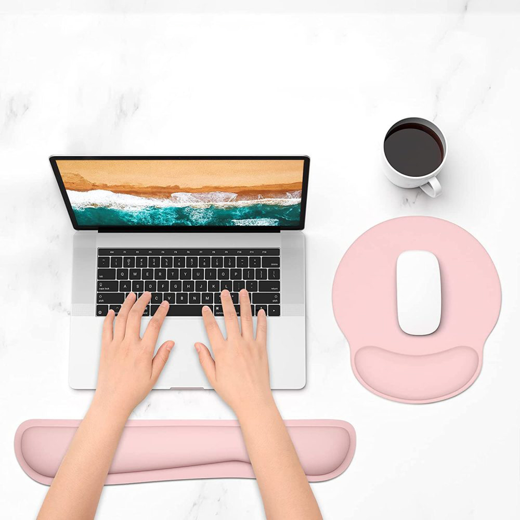 Ein Laptop mit einem Strandmotiv auf dem Bildschirm, Hände auf der Tastatur, Maus und Kaffee.