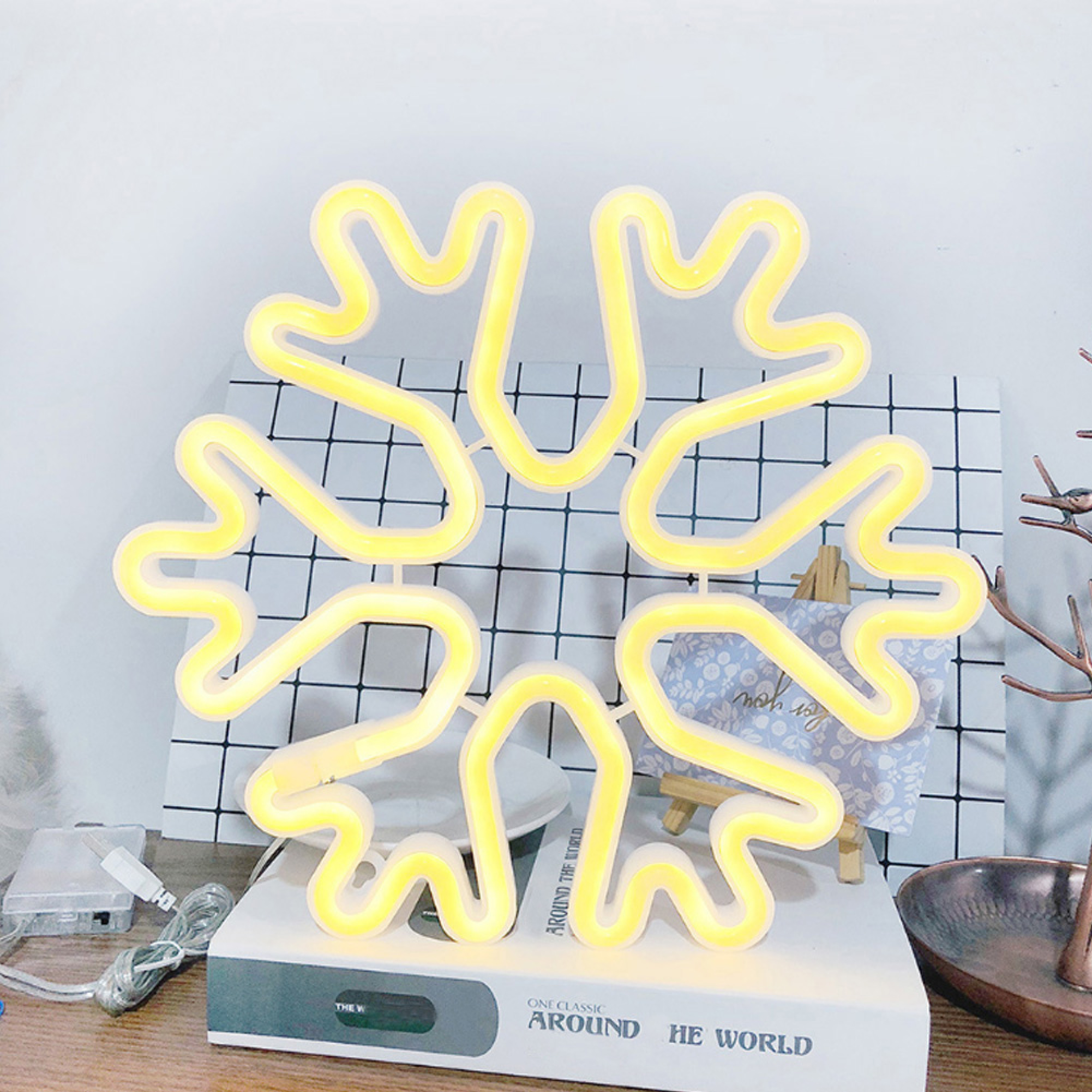 Gelbe Neon-Schneeflocken-Lampe auf einem Buch mit kariertem Hintergrund.