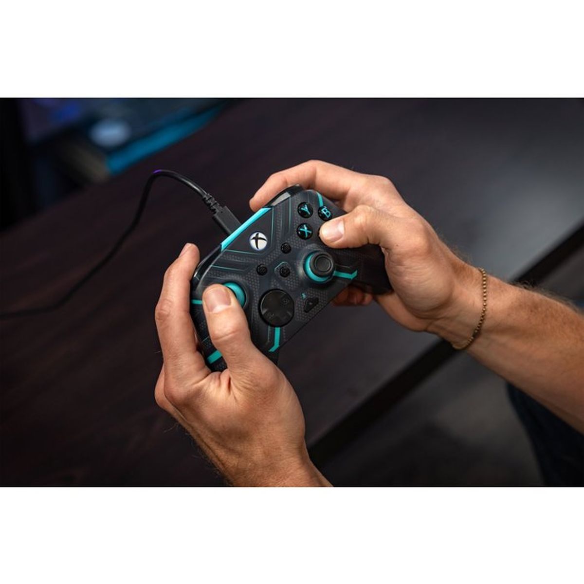 Hände halten einen schwarzen und türkisfarbenen Xbox-Controller mit eingestecktem Kabel.