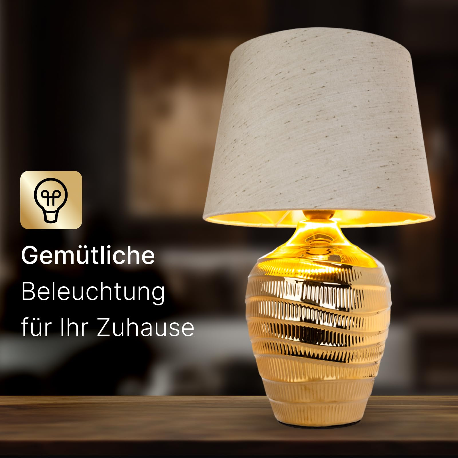 Eine goldene Metalllampe mit strukturiertem Fuß und beigefarbenem Stoffschirm steht auf einem Holztisch.