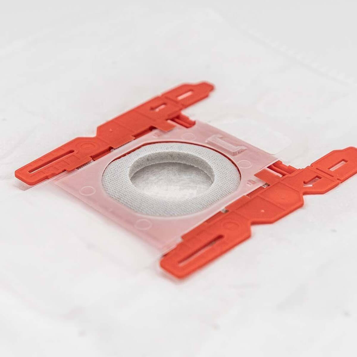 Ein rotes Plastikteil mit grauem Filter ist an einem Klarsichtbeutel befestigt.