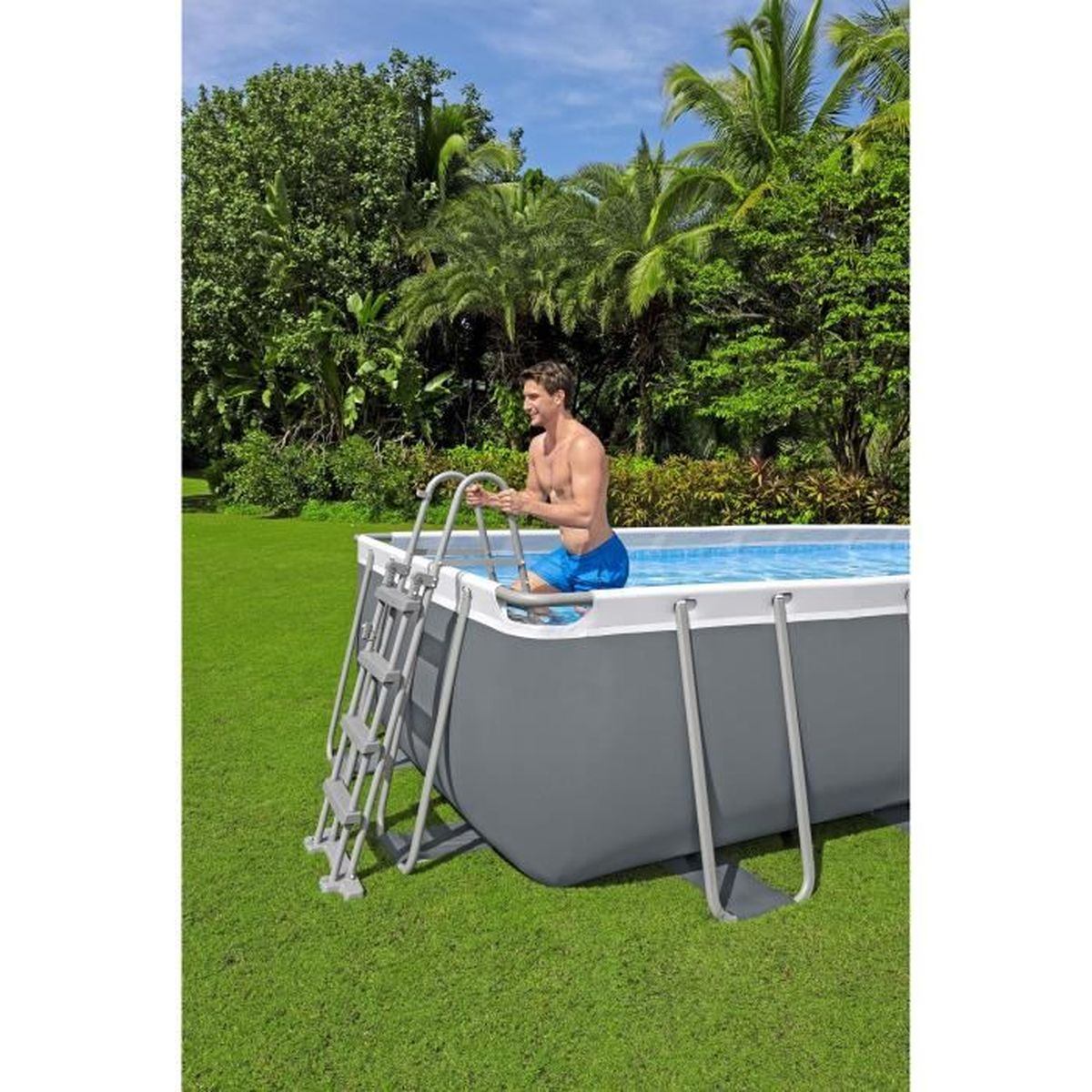 Ein Mann in blauen Badeshorts klettert auf die Leiter eines rechteckigen Pools im Freien.