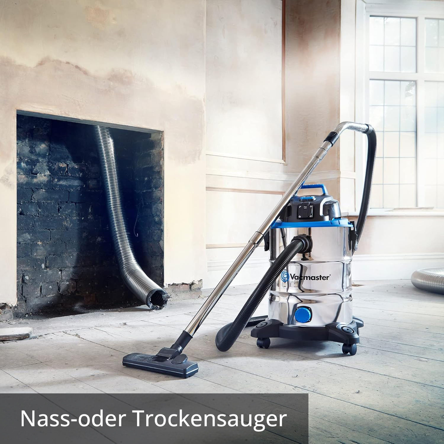 Ein Nass-/Trockensauger steht vor einem Kamin mit Schlauchanschluss auf Holzdielen.
